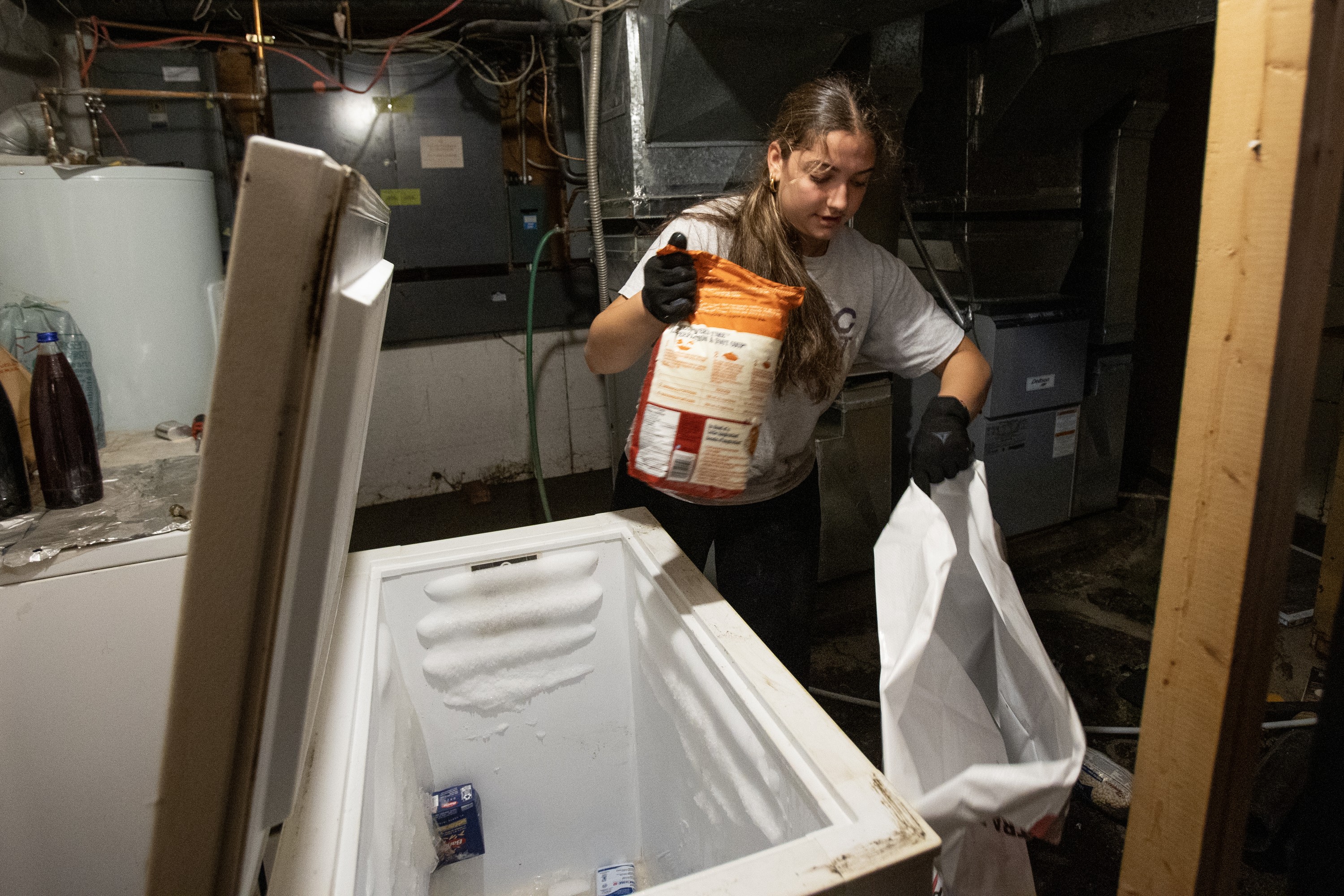 A woman clears spoiled food out of a freezer in a basement.