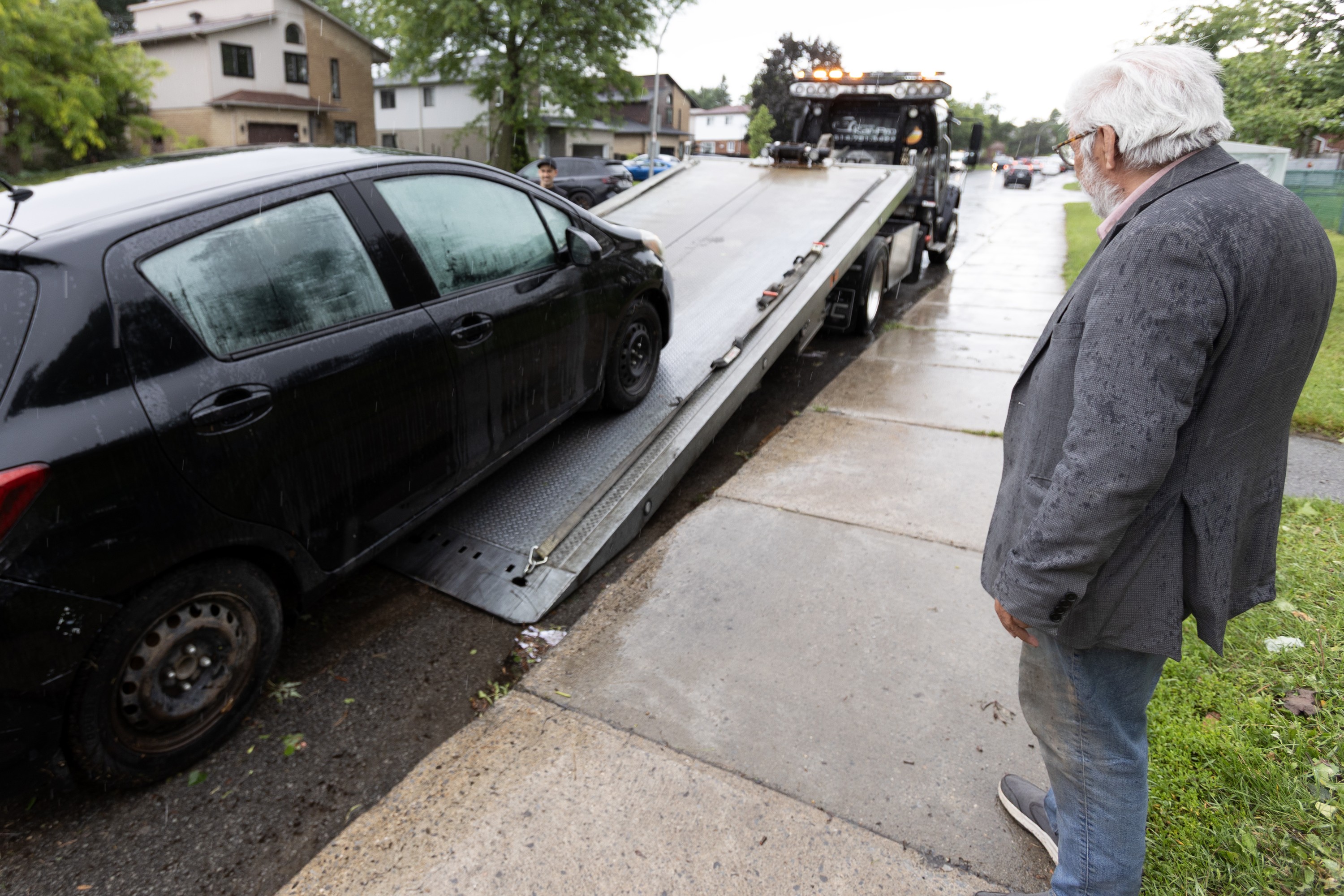 A man watches a car being loaded onto the bed of a tow truck.