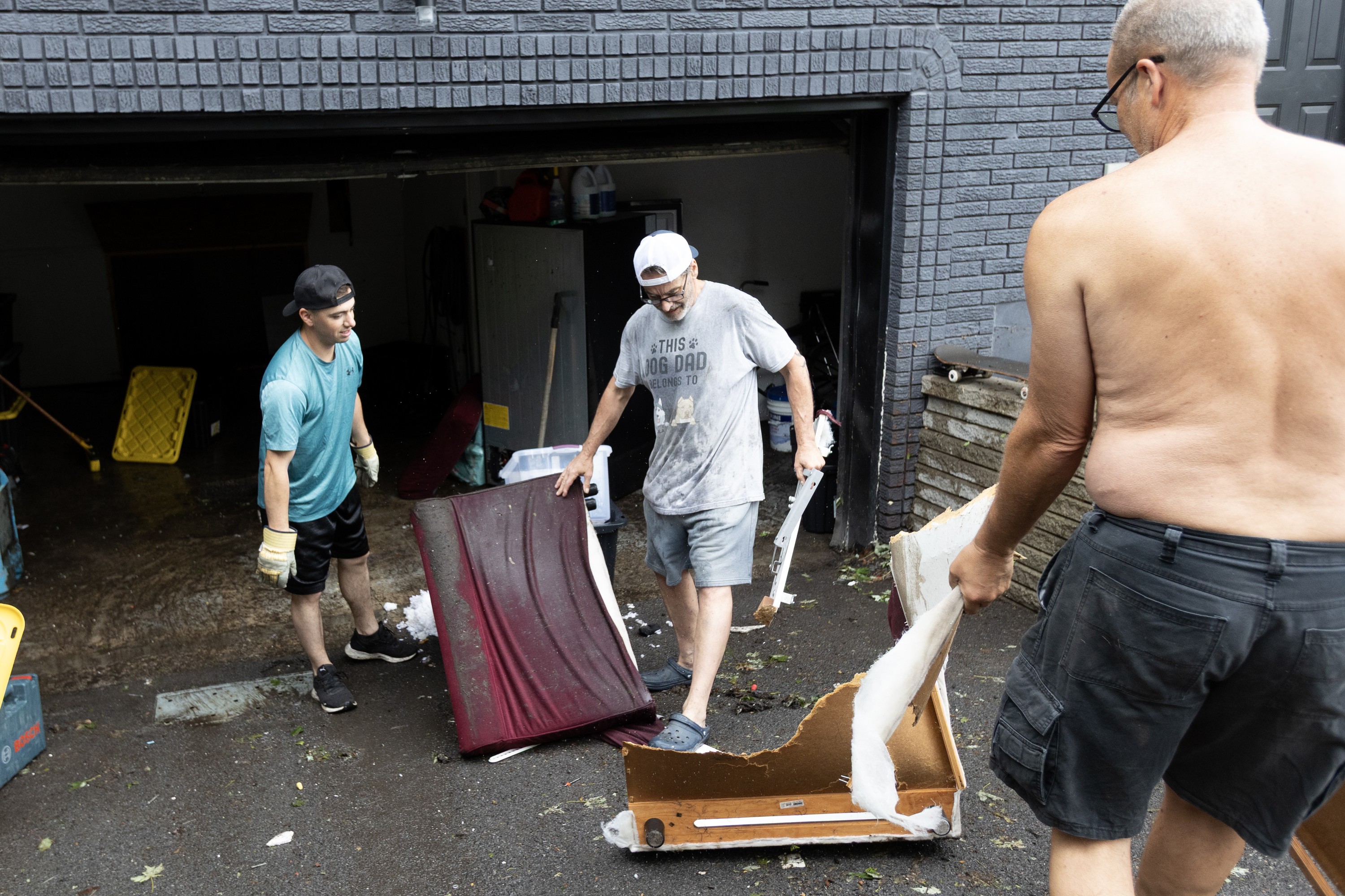 Three men carry parts of a flood-damaged couch up a driveway.