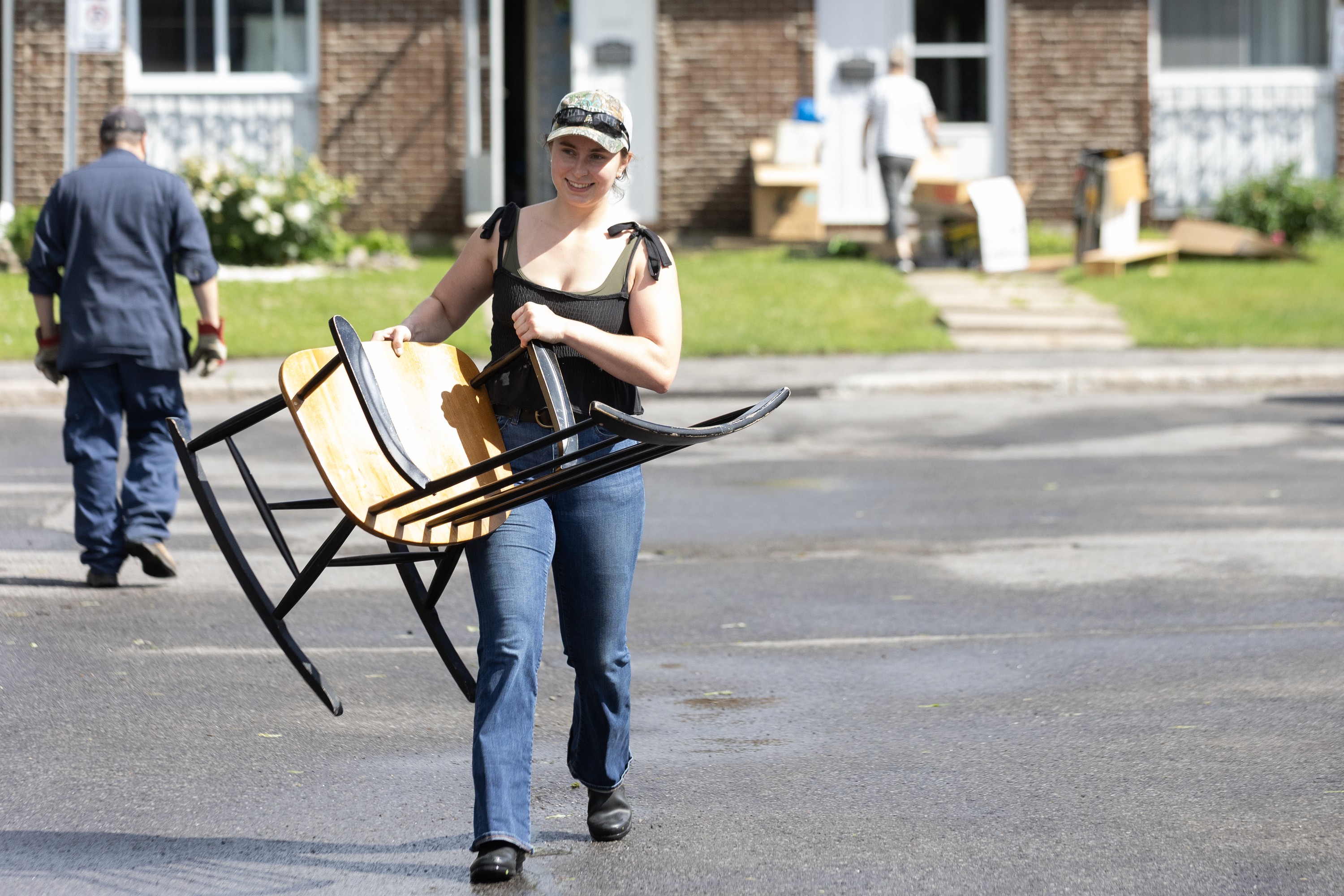 A young woman carries a chair across a street.