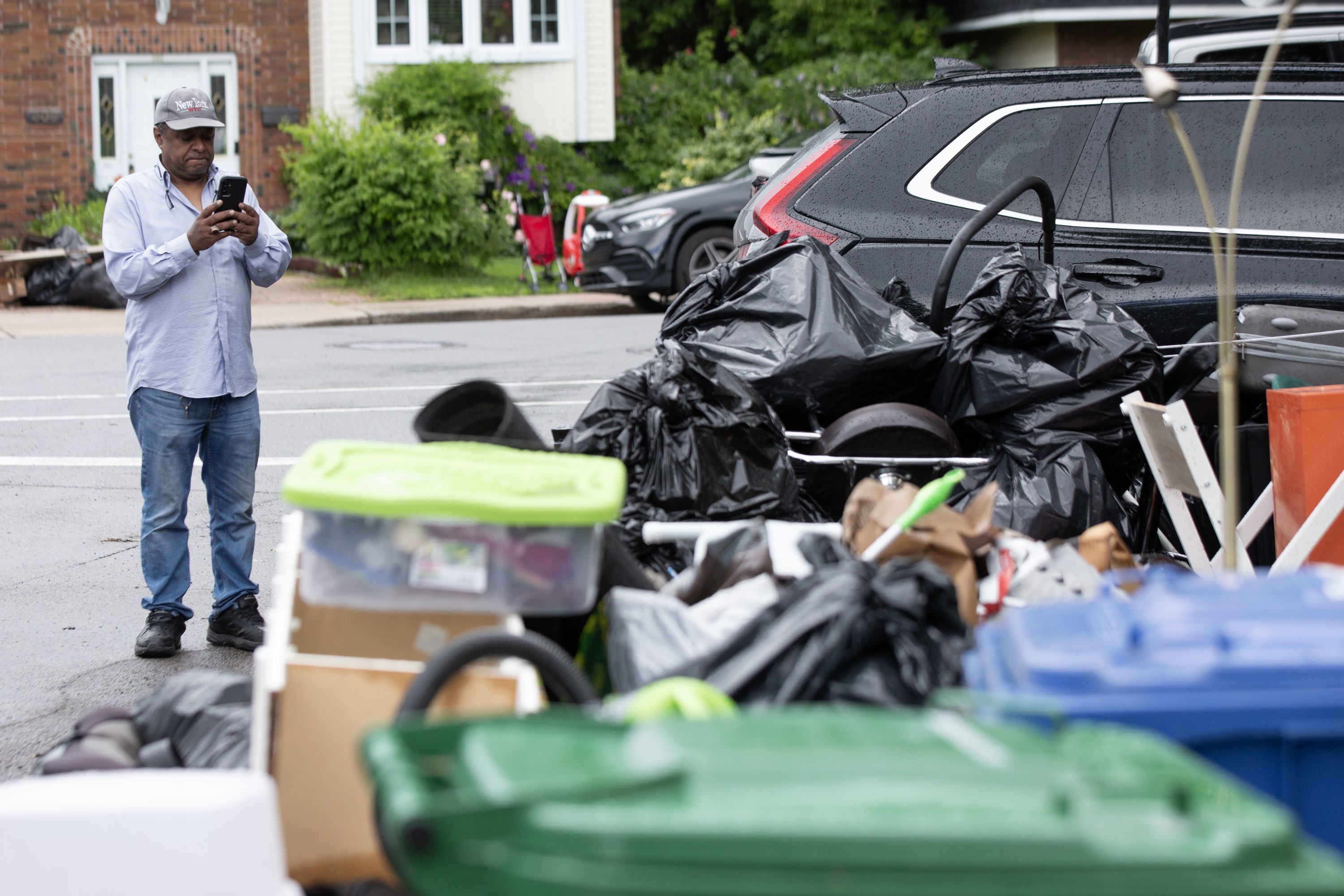 A man takes a photo of piles of garbage and flood-damaged possessions at the side of a road.