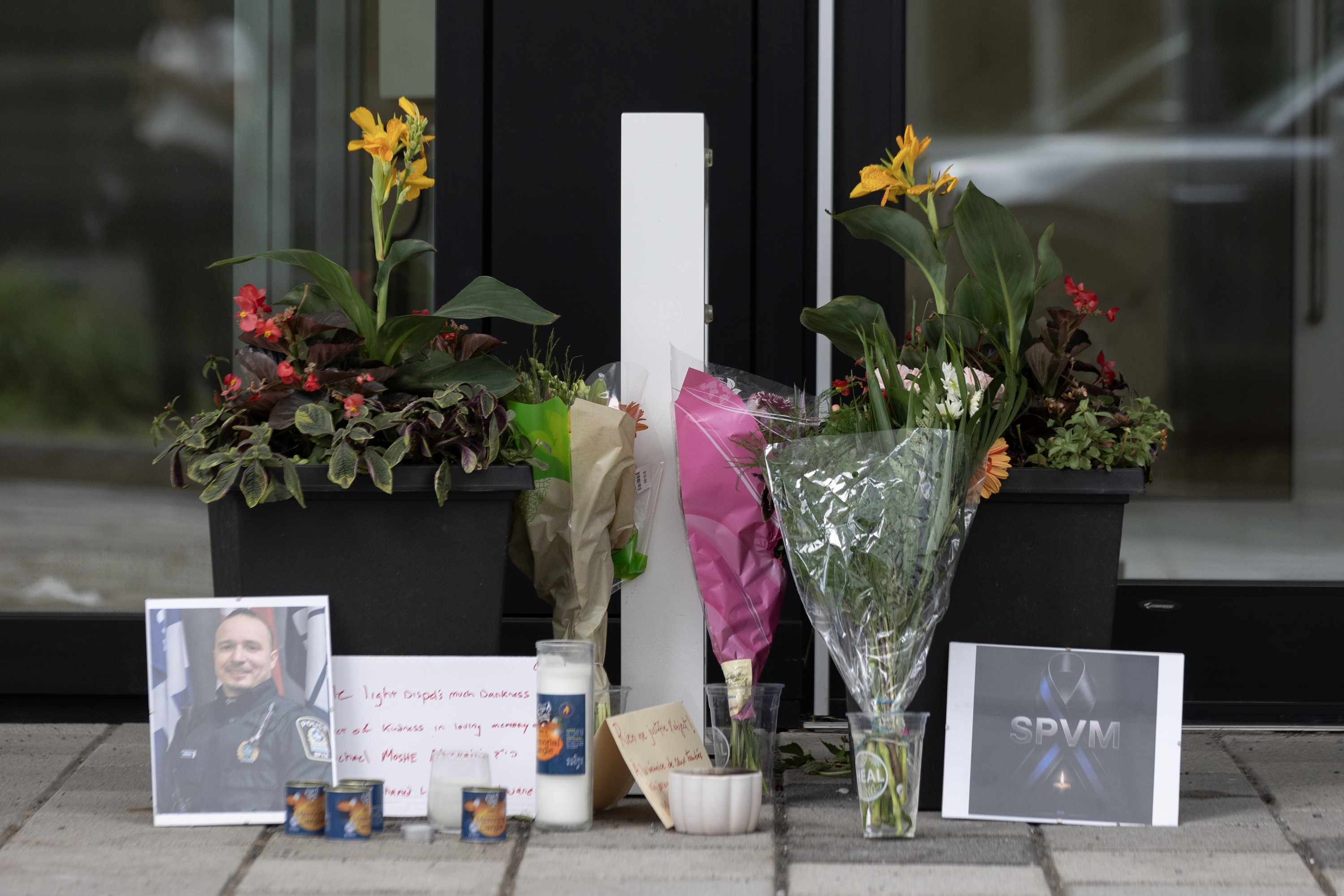 A makeshift memorial on a city street features flowers, a police officer's photo, candles and an SPVM sign.