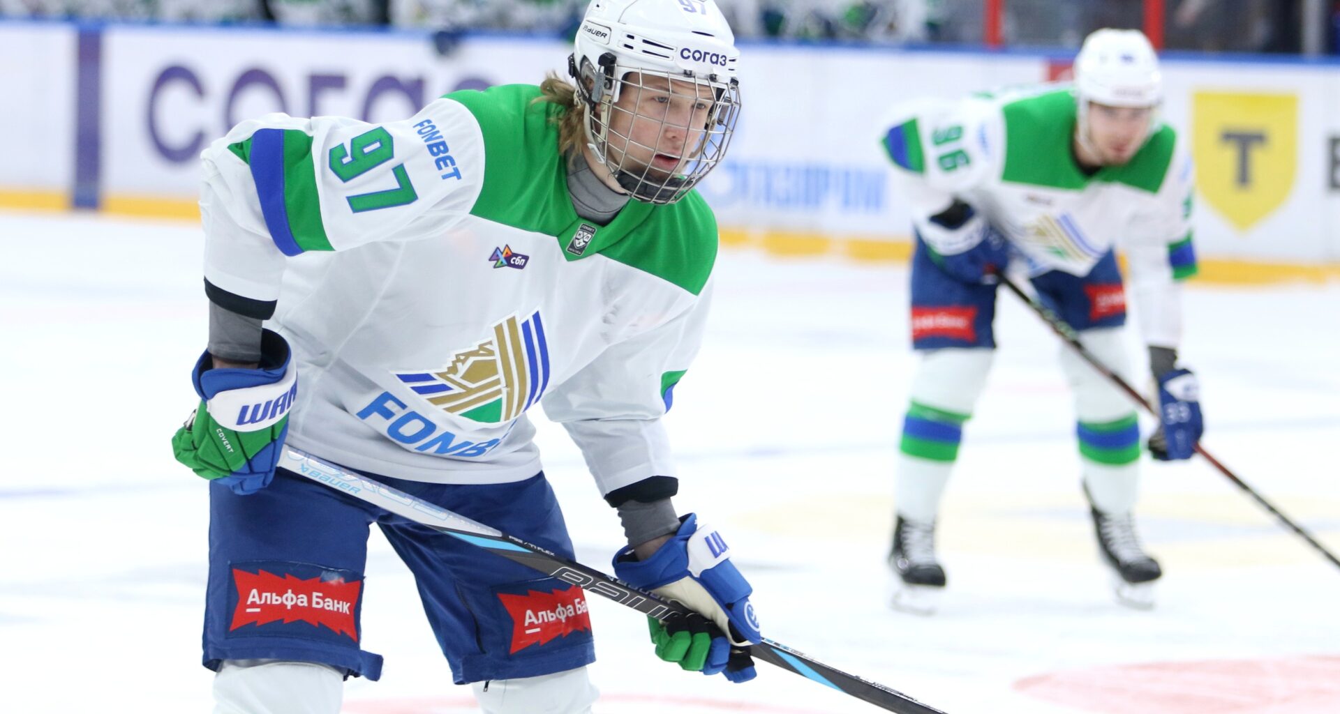 Close-up of Alexander Zharovsky wearing a white jersey with green trim on the ice during a KHL game.