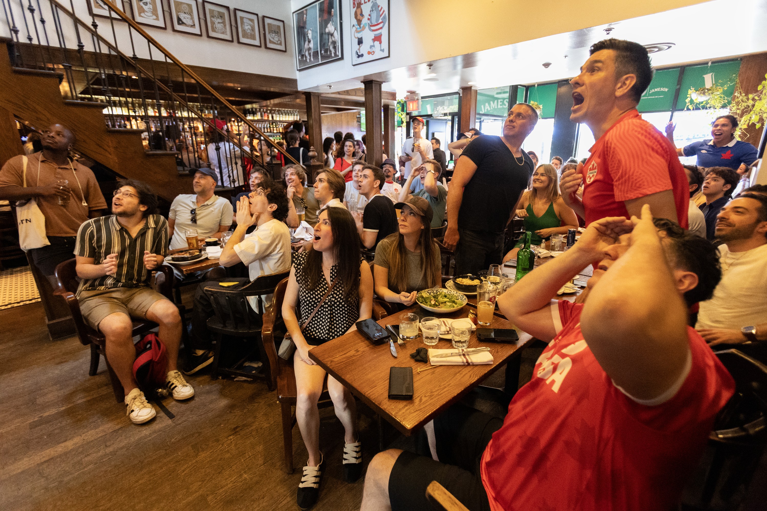 Fans are gathered in a bar watching soccer on a big screen with emotions written all over their faces.