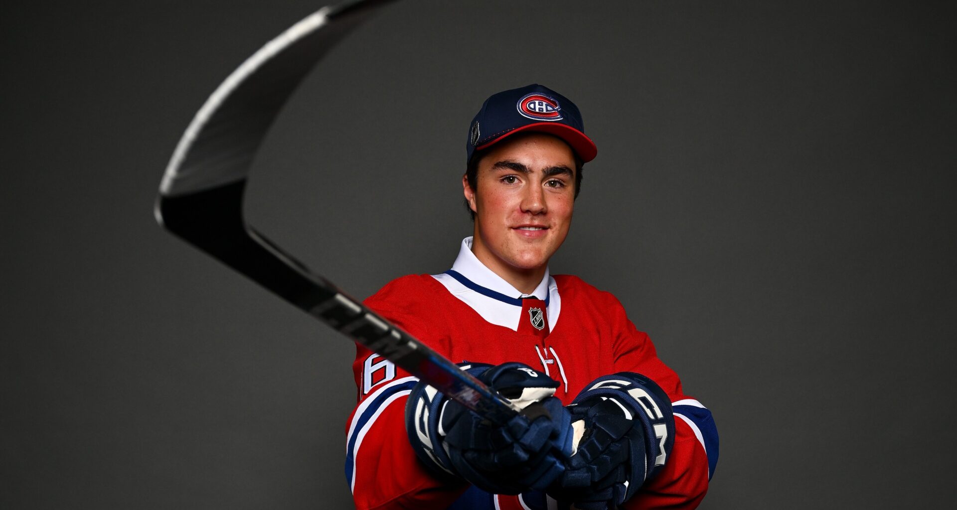 Cooper Cleaves poses for a portrait, with hockey stick extended toward the camera, after being selected by the Montreal Canadiens in the NHL Draft.