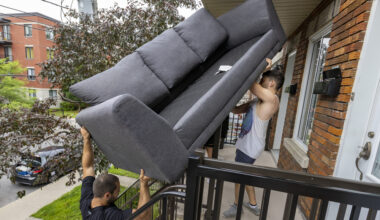Two men lift a couch up a duplex's outdoor stairs.
