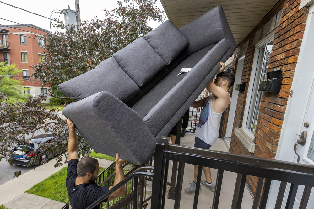 Two men lift a couch up a duplex's outdoor stairs.