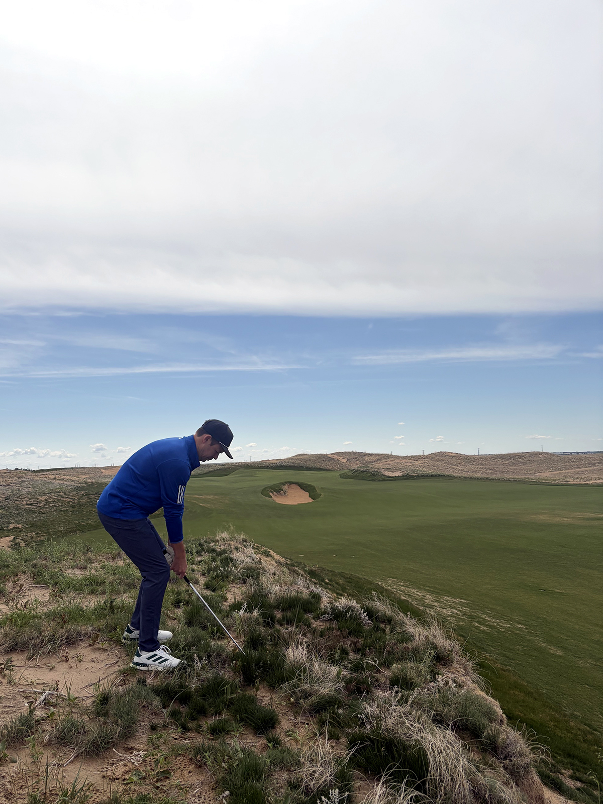 A golfer in a blue quarter-zip hits out of the rough on the eighth hole at Rodeo Dunes in Roggen, Colorado