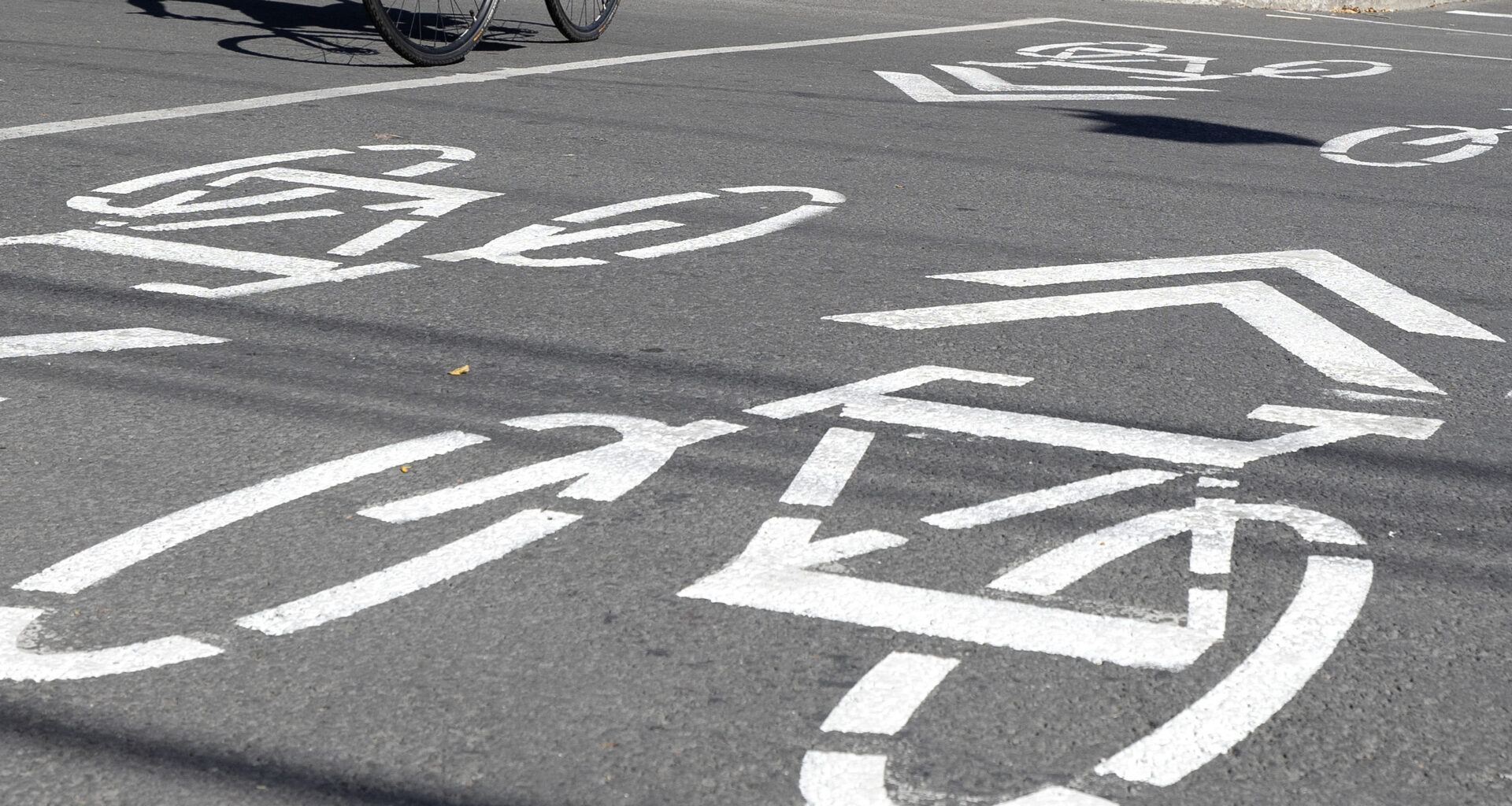 Closeup of bike-lane markings at an intersection. The wheels of a bike are visible at top left.