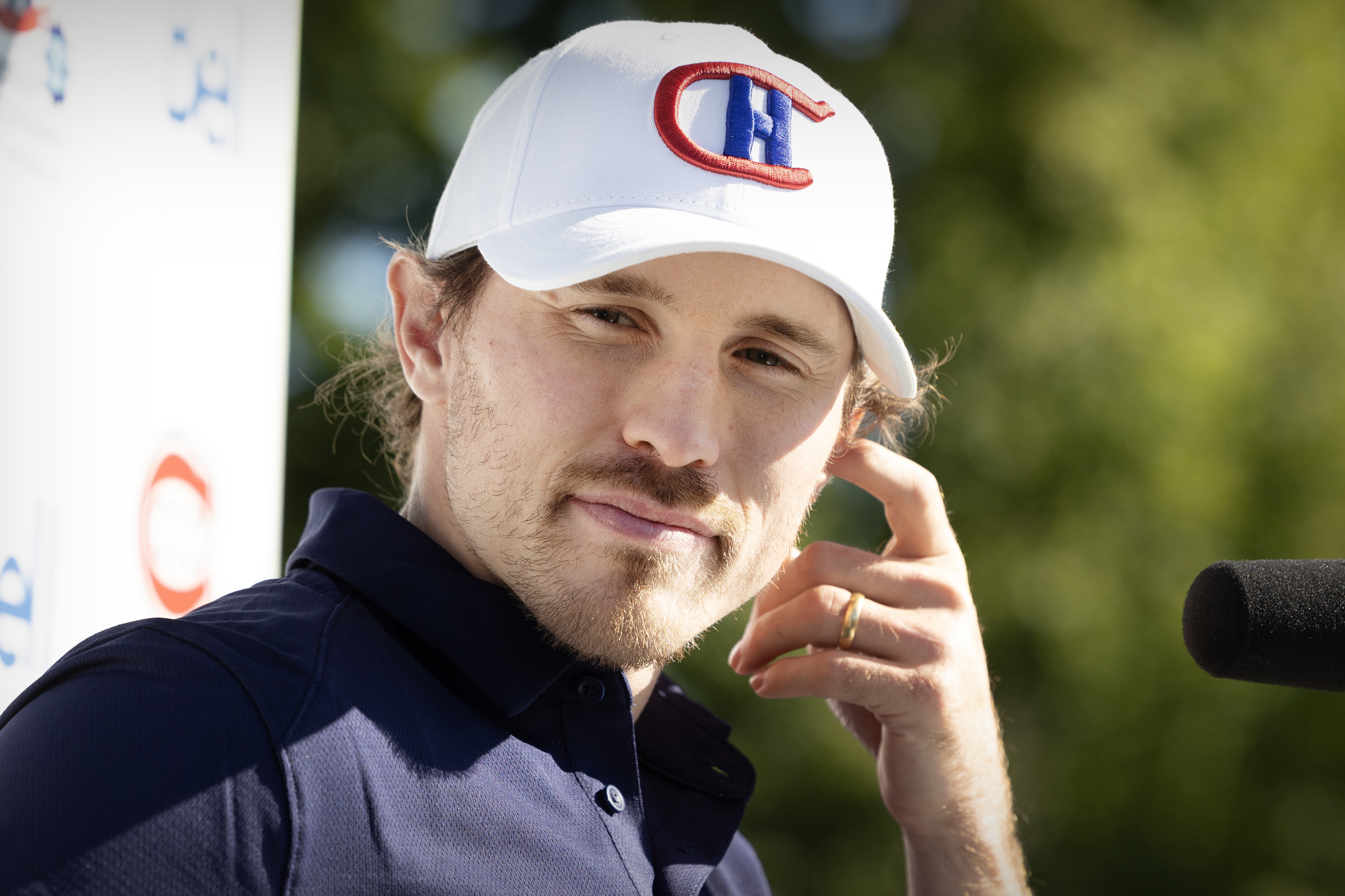 Brendan Gallagher listens while standing outside in the sun wearing a Canadiens foundation ballcap.