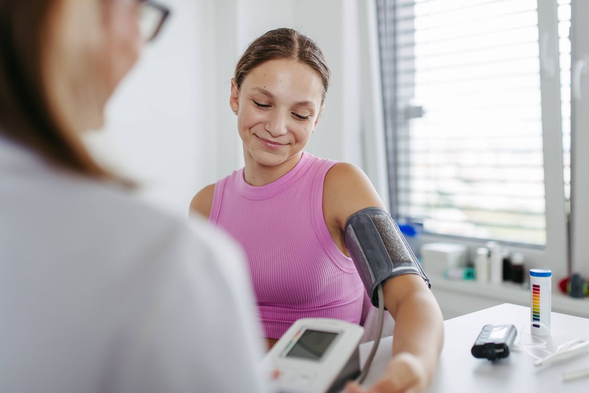 Doctor measuring a patient's blood pressure in clinic. Examining hypertension in diabetic teenage girl. Girl visiting paediatrician for annual preventive examination, check-up.