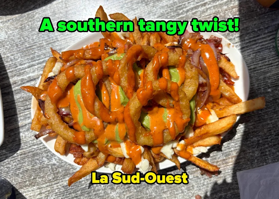 A plate of fries topped with onion rings, sauce, and pickles, set on a wooden table