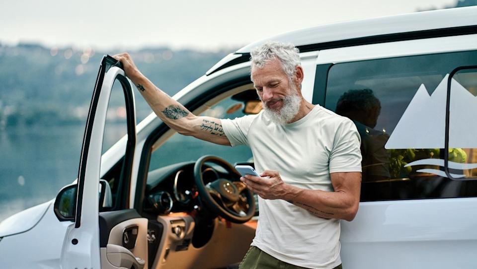 Tattooed elder man outside of car scrolling on his phone in the outdoors