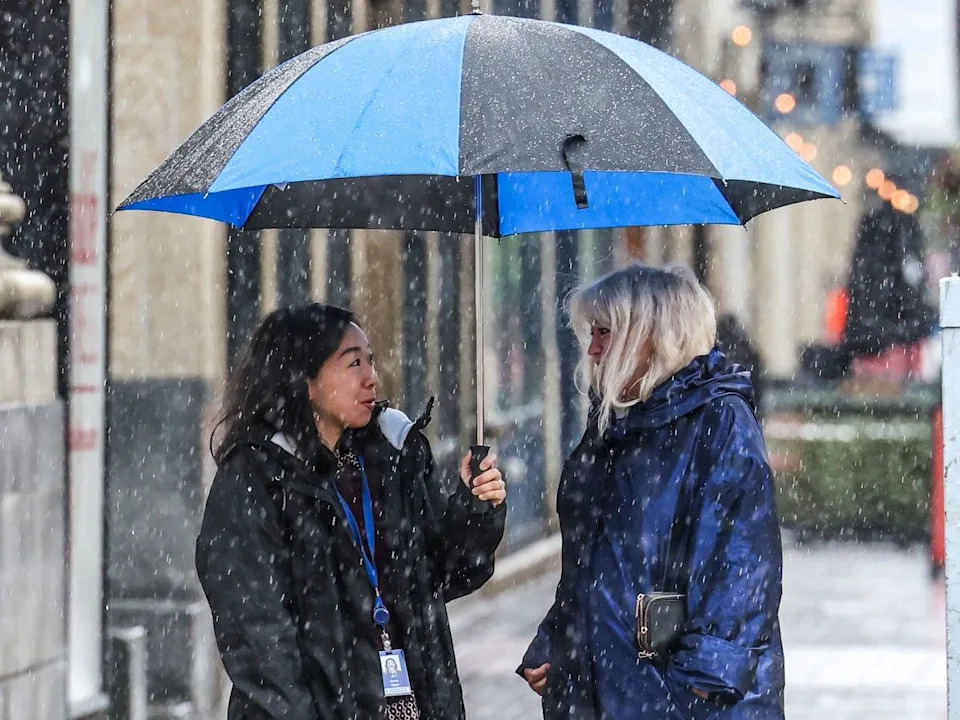 Pedestrians chat under an umbrella in the steady rain as they wait for a light to change in downtown Calgary on Monday, June 1, 2026.