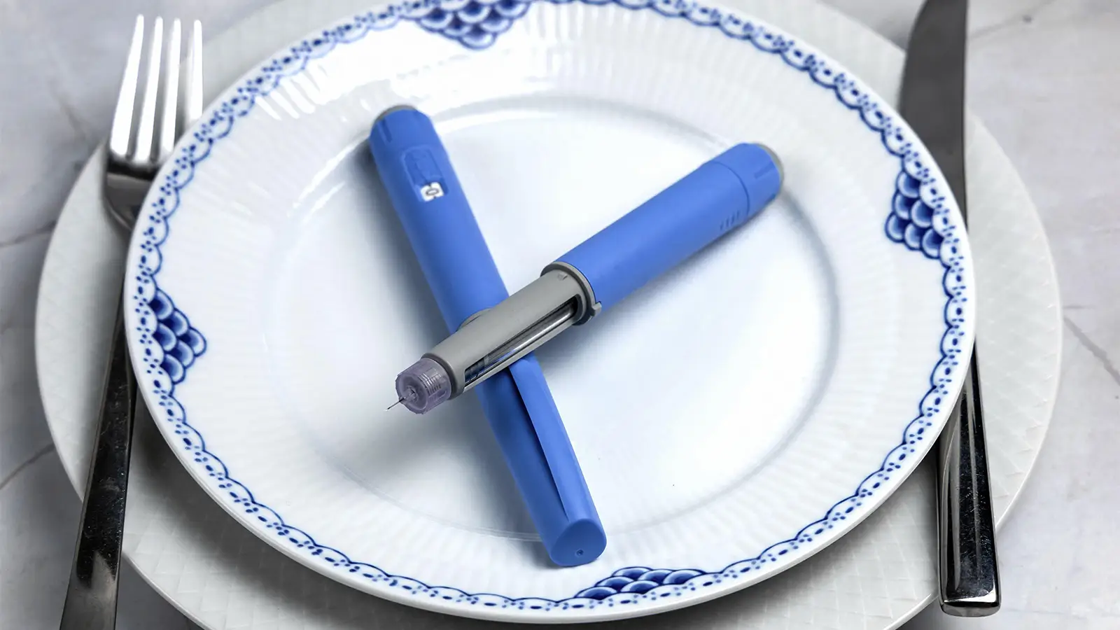 A photo of two semaglutide injection pens lying on a plate between a knife and fork.