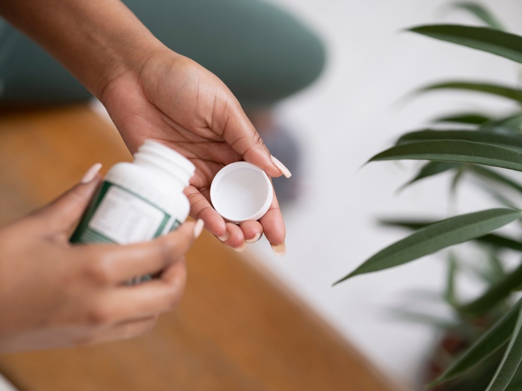 Close-up of a person holding an open bottle of pills with the lid in the other hand.