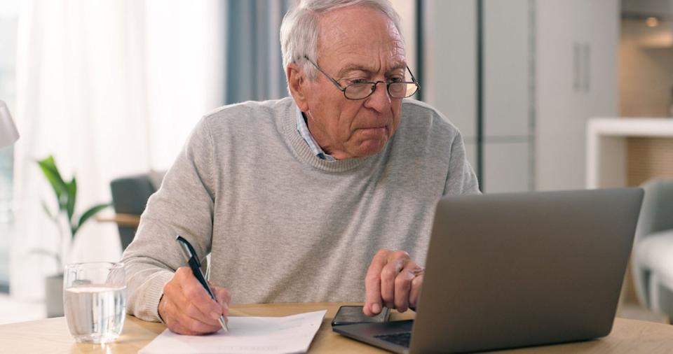 A person taking notes and looking at their laptop.