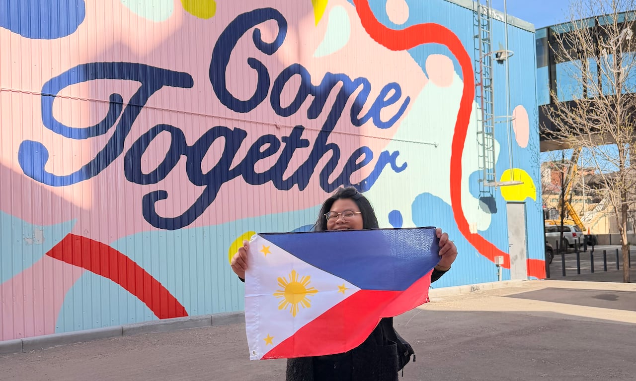 A woman standing in front of a large mural that says "come together" while holding up a Philippines flag.