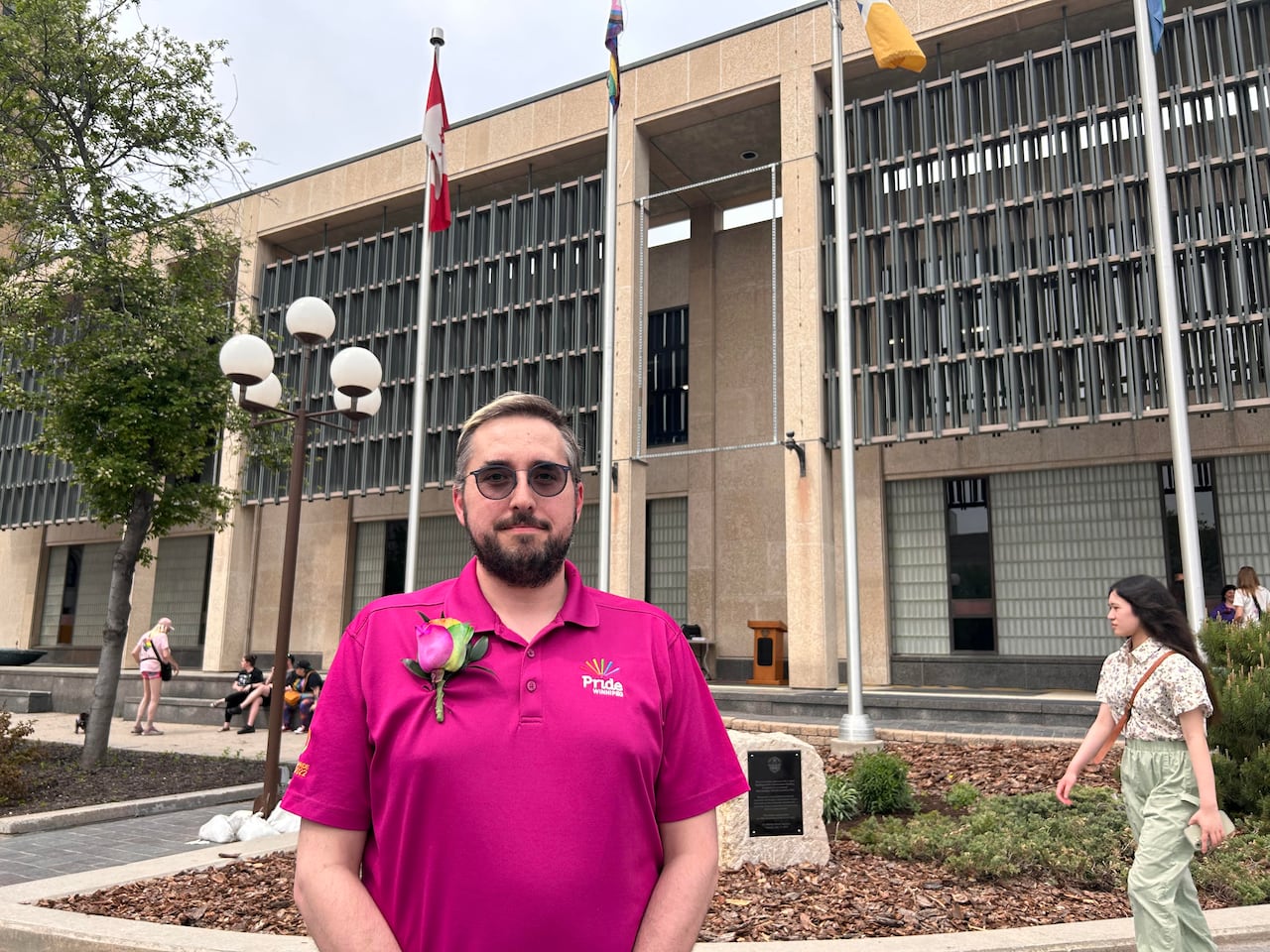 A man in a pink shirt poses in front of Winnipeg's city hall.