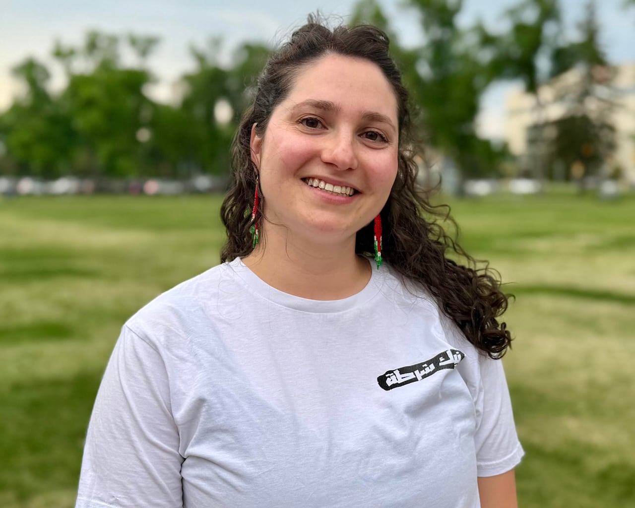 a woman with dark hair in a white shirt poses in a park in Winnipeg