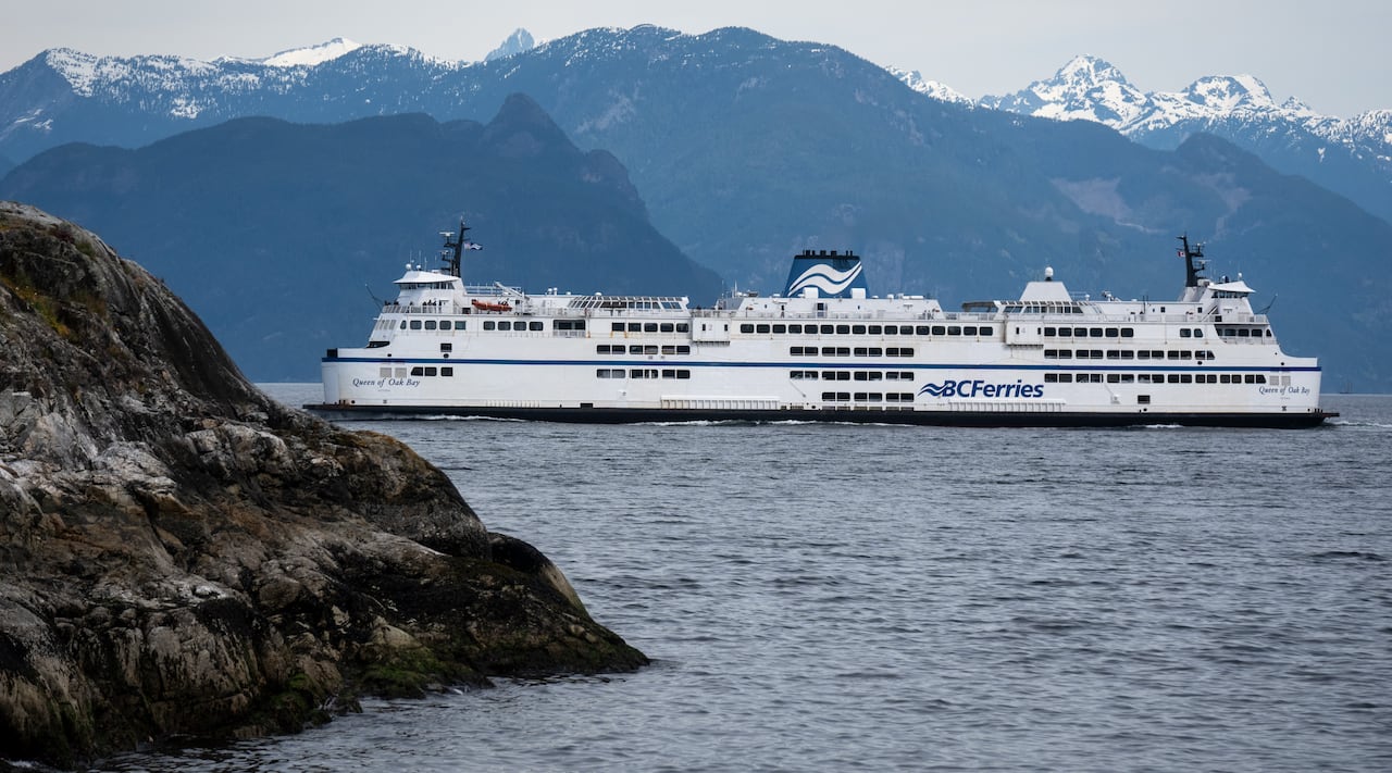 A ferry is seen in the shadow of snow-capped mountains.