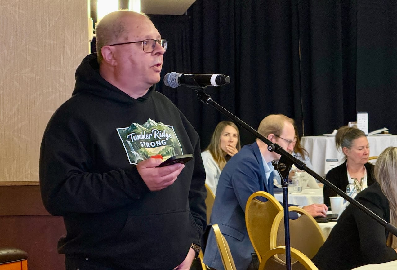 a man in a "Tumbler Ridge Strong" hoodie speaks into a microphone at a conference