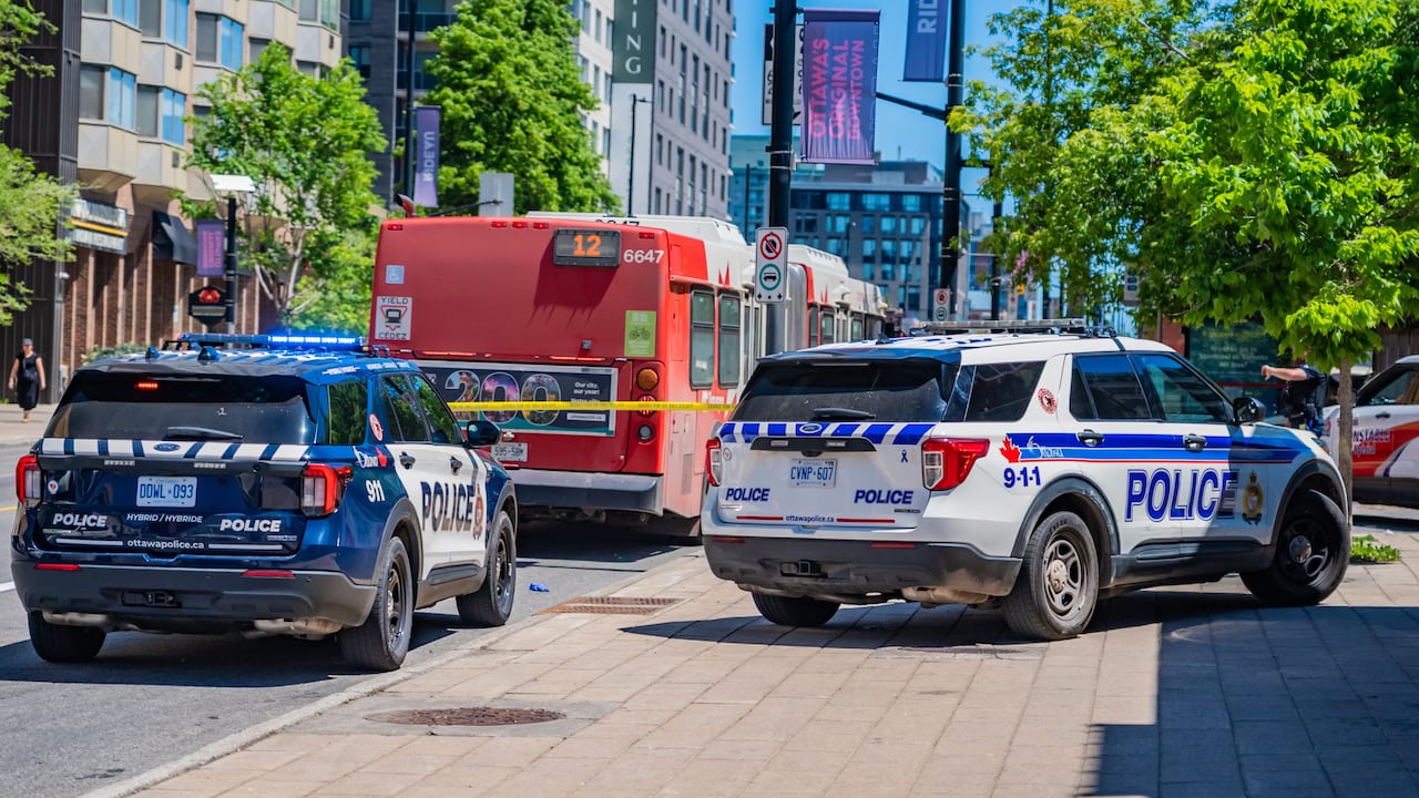 OC Transpo busses and Police cars on the road surrounded by yellow caution tape.