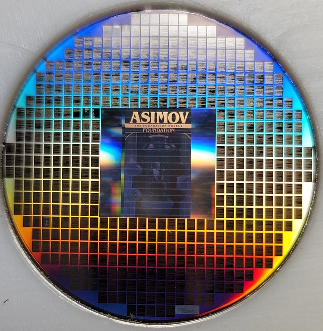 A small, circular piece of flat metal covered in dozens of black rectangles says ASIMOV on it.