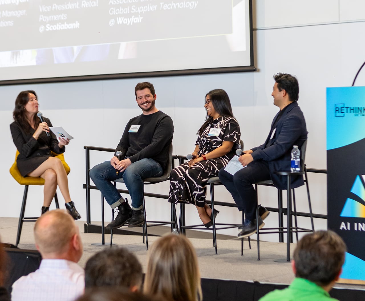 four people, two women and two men, sit in chairs on a stage taking part in a panel conversation