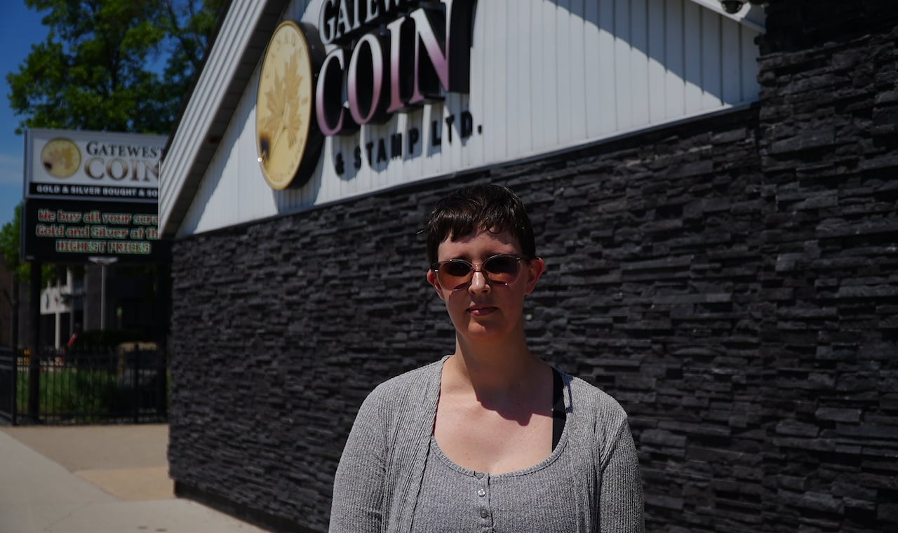 A woman standing in front of a building with a marquee that says 'Gatewest Coin & Stamp Ltd.'