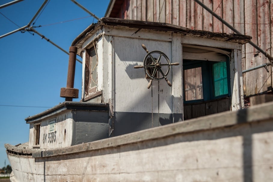 A close-up photo shows the cabin of an old wooden fishing boat, with a small steering wheel mounted on the outside wall.