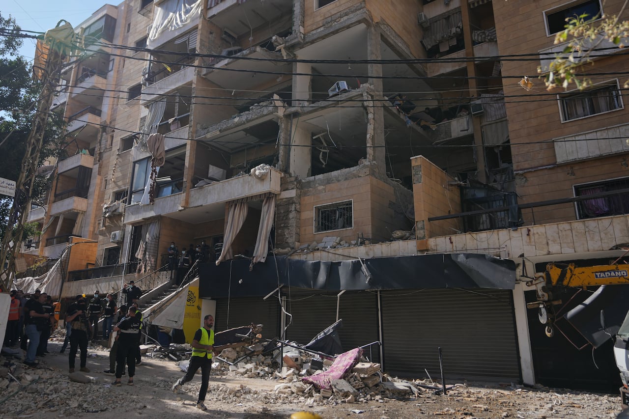 People walk in front of a damaged building.