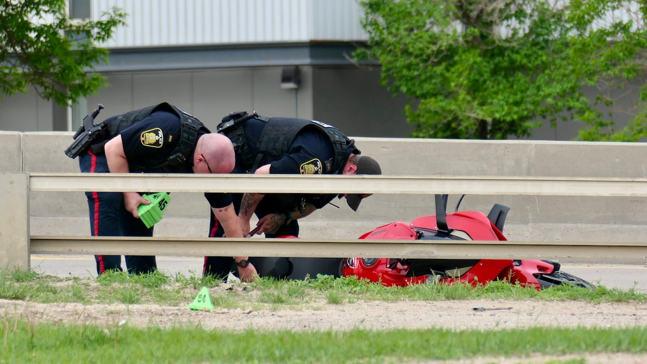 Two police officers bend down to place colourful pylons around an overturned red motorcycle on a city road