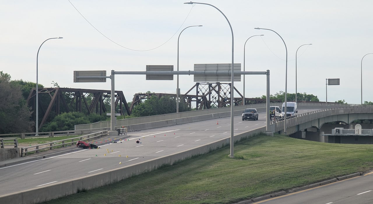 A motorcycle is overturned on an empty city bridge, surrounded by colourful pylons and several police vehicles