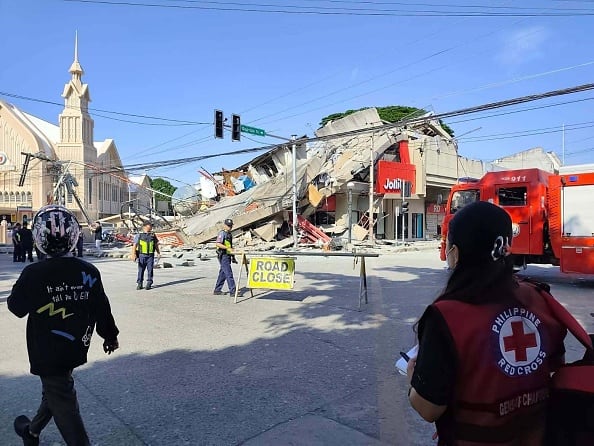 A collapsed building is shown on an urban street. Rescue workers are shown in the foreground.