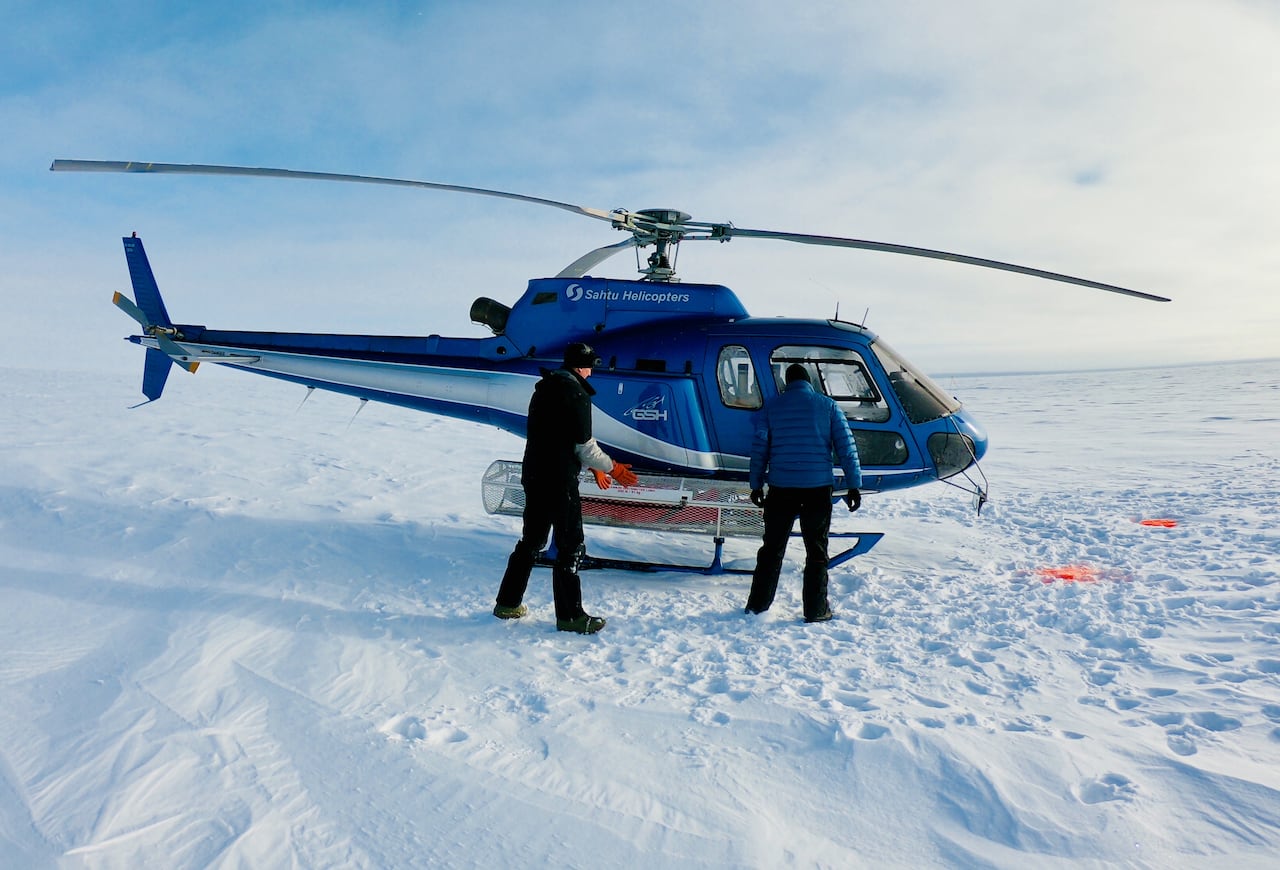 Two people standing in front of a helicopter on a barren, snow-covered landscape.