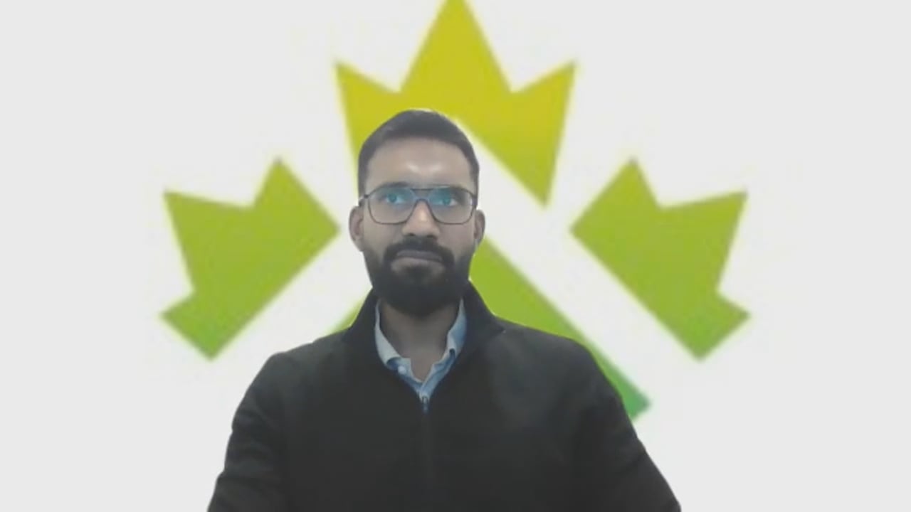 An Indian man sits in front of a logo.