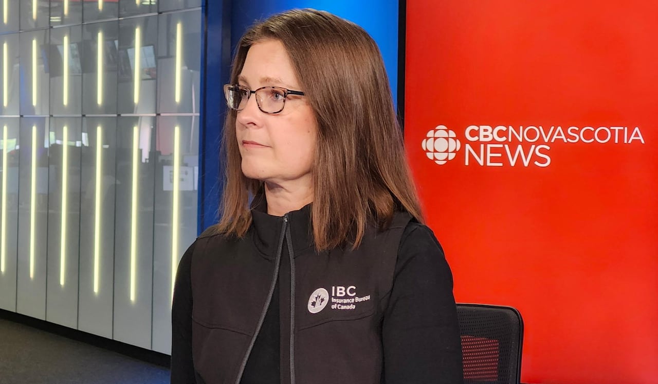 A woman with glasses and brown hair is interviewed on a television news set.
