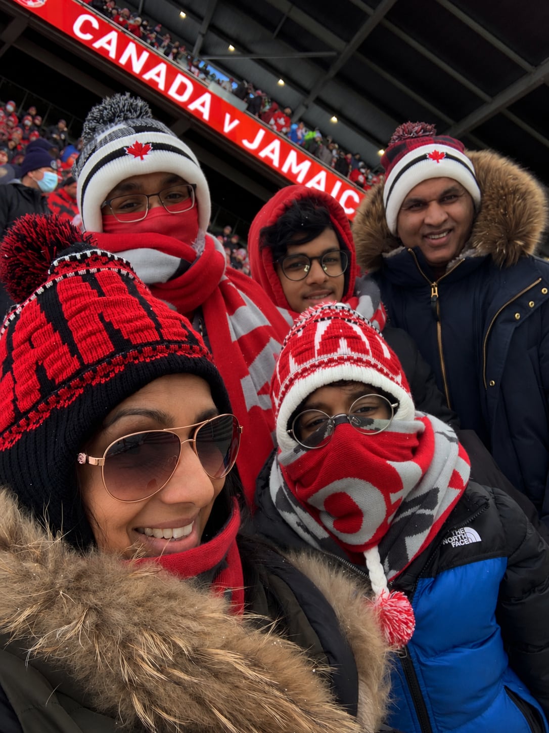 A family wearing team Canada attire takes a selfie at BMO stadium during a Team Canada soccer match.