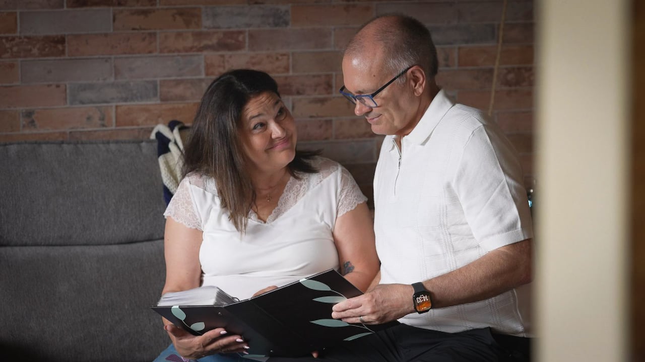 Two people sit on a couch and look through a photo album.