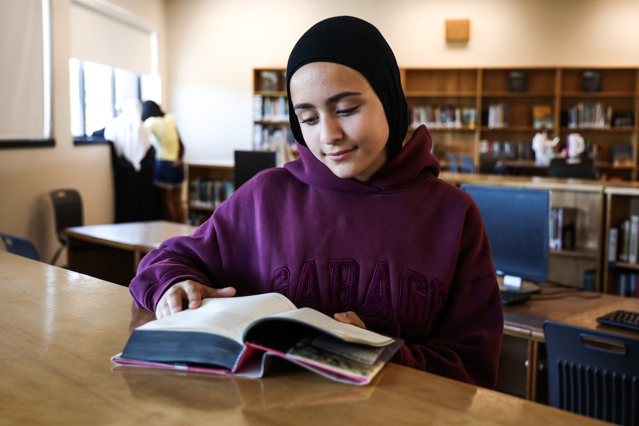 A girl wearing a purple sweater stares at a book.