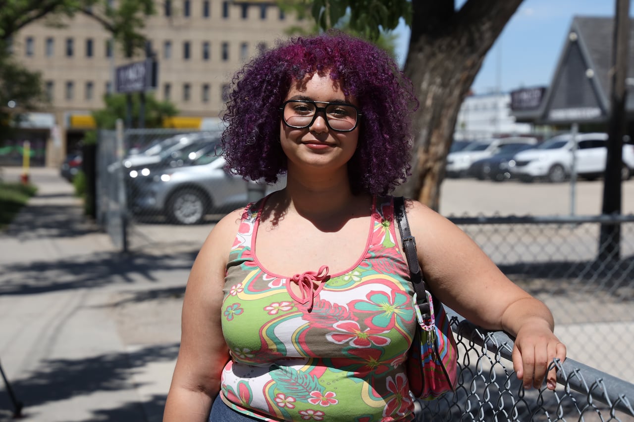 A girl with purple hair lays her arm on a metal fence.