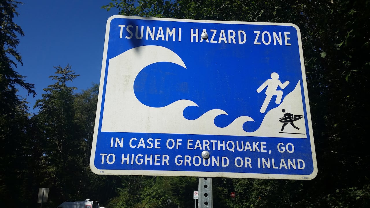 A sign that says 'Tsunami Hazard Zone. In case of earthquake, go to higher ground or inland.'