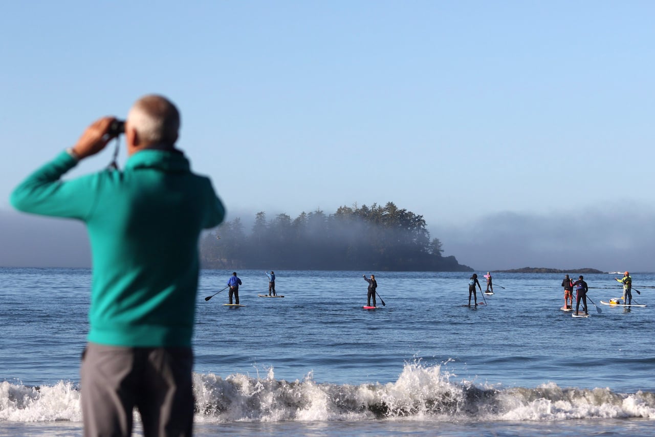 A man looks out at paddle boarders with binoculars