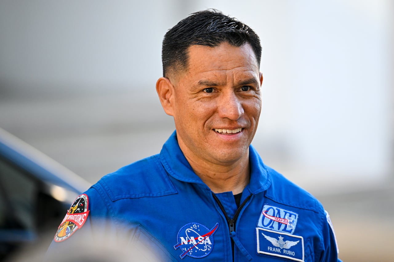 An astronaut in a blue jumpsuit smiles at the camera.