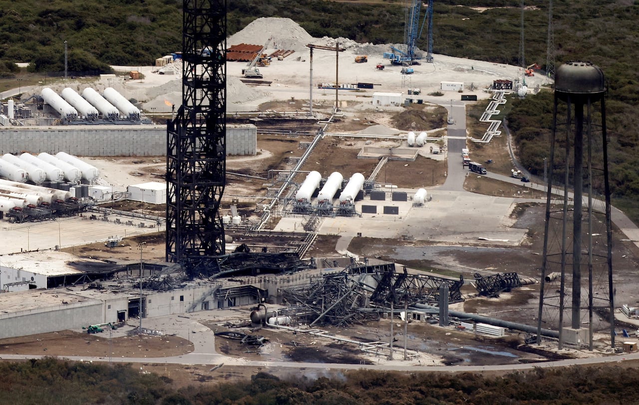 A blackened, burned out metal tower stands over the scorched ground of a rocket launchpad a day after an explosion.
