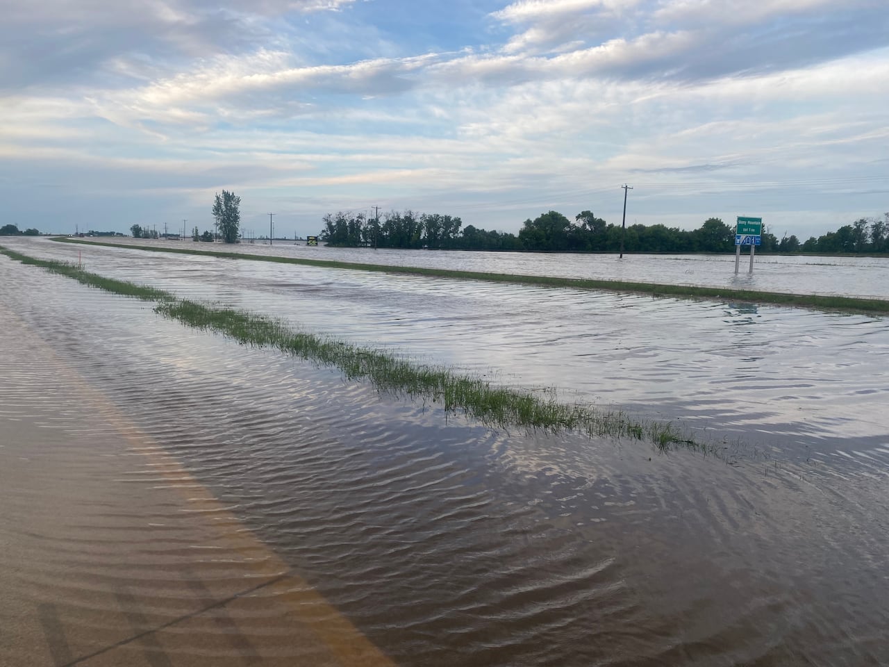 A flooded highway with the sign looking like it's standing in a lake