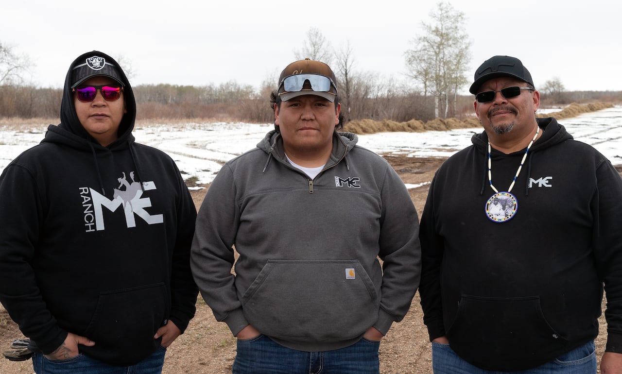 Three men, stand side by side, with two men on each end wearing hooded sweaters and one in middle wearing a dark jacket.