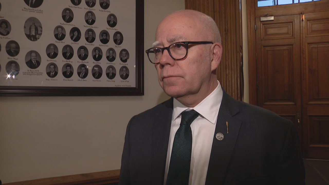 A bald man wearing glasses stands in a legislature building.