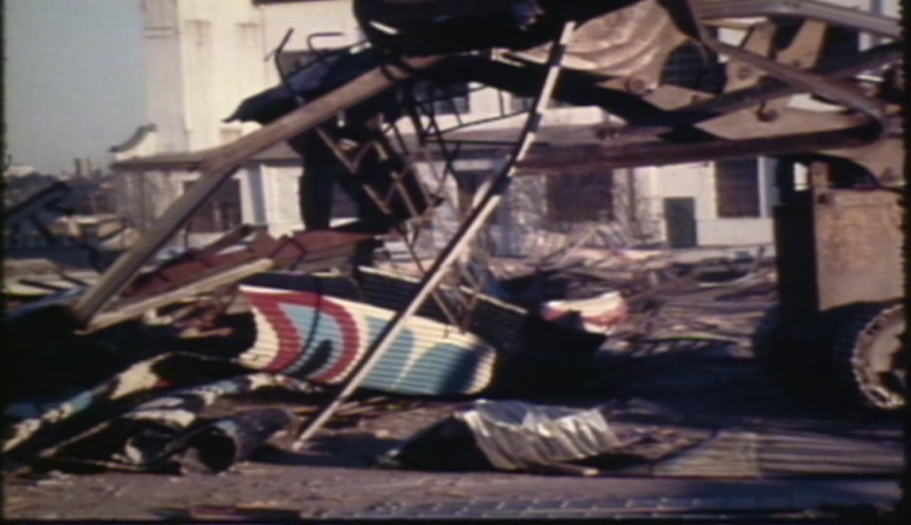 Scraps of metal with Haida designs are under demolition by a tractor in a vintage news still frame.